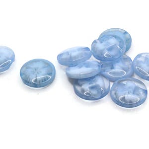 Puede incluir: Un conjunto de cuentas de vidrio azul claro y blanco veteado. Las cuentas de forma ovalada tienen una superficie ligeramente abovedada. Las cuentas translúcidas están dispersas sobre un fondo blanco. Estas cuentas son adecuadas para la fabricación de joyas y manualidades.