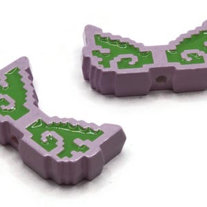 May include: Two lavender-colored, pixelated, decorative objects with green, swirled designs. The objects have a curved shape and appear to be made of a glossy material. They are likely decorative elements or components of a larger design.