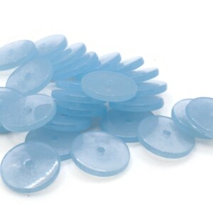 May include: A pile of light blue round buttons with a hole in the center. The buttons are made of a smooth, translucent material.