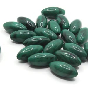 May include: A collection of oval-shaped, polished malachite beads. The beads are a deep, rich green with darker green marbling and a glossy finish. They are scattered on a white surface, showcasing their natural patterns.