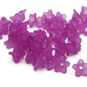 Puede incluir: Un gran grupo de cuentas de plástico de color púrpura con forma de flor. Las cuentas son translúcidas y tienen un acabado mate.