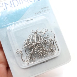 May include: A package of silver-colored earring hooks. The package is clear plastic, and the backing is light blue with the word "FINDINGS" at the top. The package also says "earrings" and "boucle d'oreille".