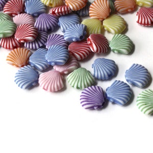 Op de afbeelding: Een verzameling kleurrijke plastic schelp kralen met witte strepen. De kralen zijn willekeurig gerangschikt op een witte achtergrond.