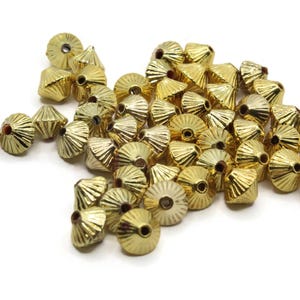 Puede incluir: Un montón de cuentas de metal de color dorado con forma de cono y diseño acanalado. Las cuentas tienen un agujero en el centro para enhebrar.
