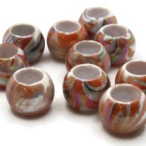 Puede incluir: Un grupo de 10 cuentas de plástico de colores con patrones de espiral. Las cuentas son una mezcla de naranja, blanco y marrón con un ligero brillo iridiscente. Las cuentas son redondas y tienen un agujero en el centro.