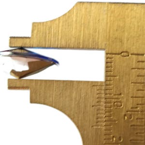 May include: A close-up of a round, clear glass object being measured with a brass caliper. The caliper shows a measurement of 1.5 inches.