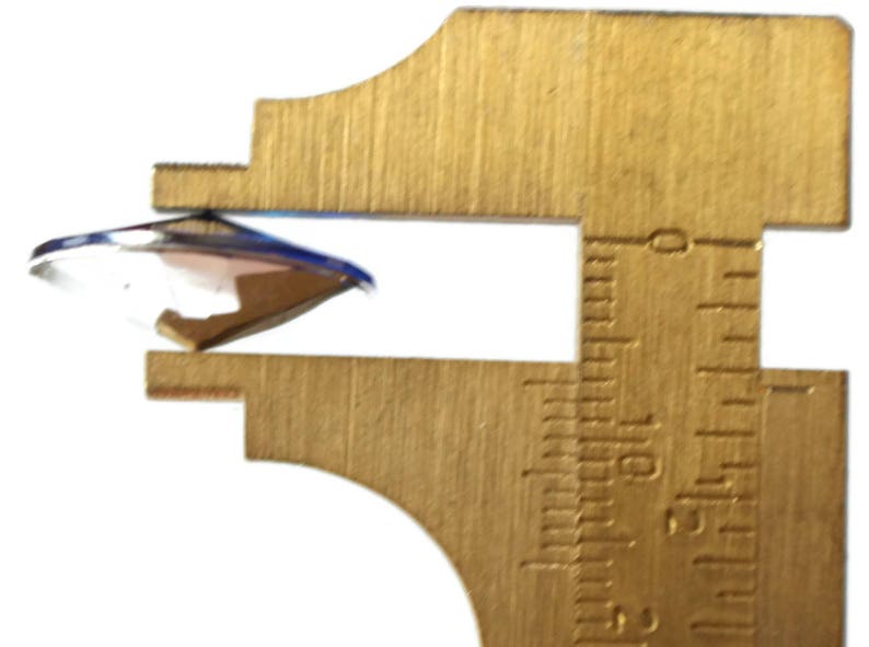 May include: A close-up of a round, clear glass object being measured with a brass caliper. The caliper shows a measurement of 1.5 inches.
