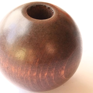 May include: A dark brown wooden bead with a hole in the center. The bead is smooth and polished.