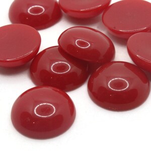 May include: A group of ten red round cabochon glass gems. The gems are smooth and shiny.