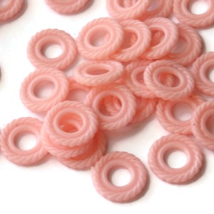 May include: A pile of pink plastic rings with a rope-like texture. The rings have a small hole in the center.