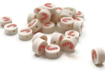 Puede incluir: Un montón de cuentas de cerámica blanca con diseños de bastones de caramelo rojos. Las cuentas tienen un agujero en el centro para enhebrar.