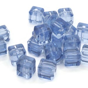 Puede incluir: Un grupo de cuentas cuadradas de vidrio azul claro con un agujero en el centro de cada cuenta.