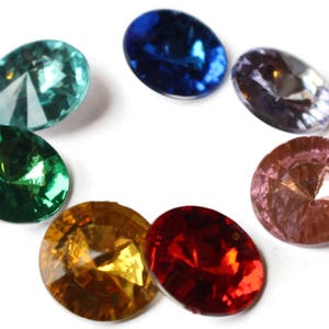 May include: Seven round, faceted, glass gems in various colors. The gems are arranged in a circle on a white background. The colors are teal, green, blue, purple, pink, red, and yellow.