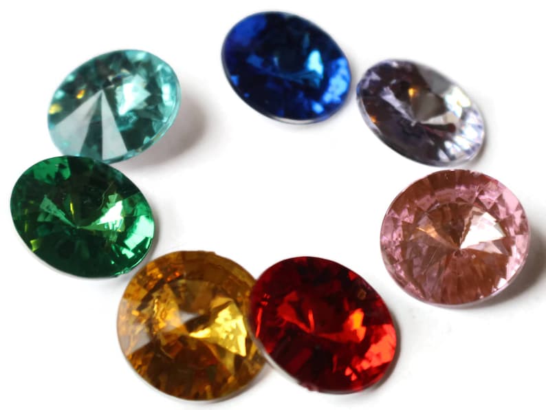 May include: Seven round, faceted, glass gems in various colors. The gems are arranged in a circle on a white background. The colors are teal, green, blue, purple, pink, red, and yellow.