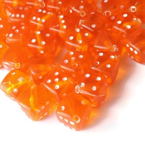 May include: A pile of orange dice with white dots. The dice are made of clear plastic and are scattered on a white surface.
