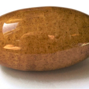 Puede incluir: Una cuenta de cerámica marrón con un esmalte moteado. La cuenta es lisa y de forma ovalada.