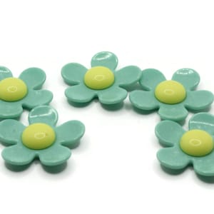 May include: Five green plastic daisy-shaped buttons with yellow centers.