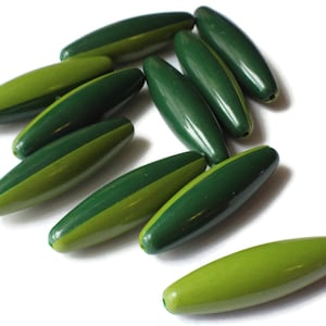 Puede incluir: Un grupo de diez cuentas ovaladas de color verde y verde claro. Las cuentas están hechas de madera y tienen un acabado brillante.