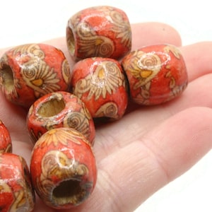 May include: A close-up of a group of wooden beads with a floral pattern. The beads are orange with a light brown floral design. The beads are approximately 2.5 cm in diameter.
