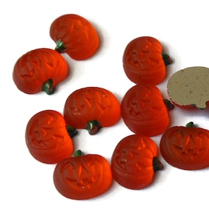 May include: Ten orange glass pumpkin-shaped cabochons with a carved jack-o'-lantern face. The cabochons are approximately 1 inch in diameter.
