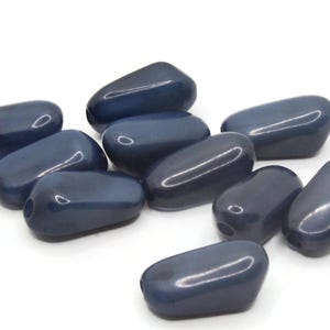 Op de afbeelding: Een groep van tien gladde, donkerblauwe, ovale kralen. De kralen zijn glanzend en hebben een lichte glans.