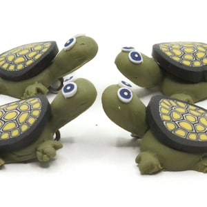 Pode incluir: Quatro estatuetas de tartarugas verdes e pretas com detalhes amarelos e olhos azuis. As tartarugas são feitas de argila polimérica e têm uma carapaça texturizada.