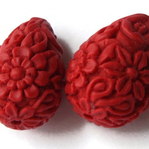 May include: Two red teardrop-shaped beads with a floral design. The beads are made of a smooth, textured material.