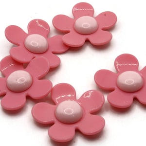 May include: Pink flower-shaped embellishments with a light pink center. These decorative floral accents are ideal for crafting projects, scrapbooking, or adding a touch of whimsy to various designs. The flowers are approximately 1 inch in diameter.