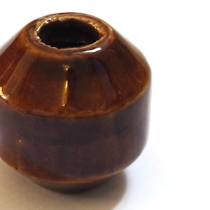May include: A brown ceramic insulator with a round shape and a hole in the center.