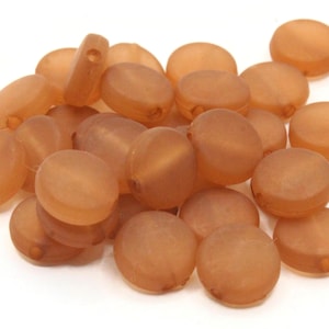 May include: A pile of round, flat, brown beads with a hole in the center. The beads are made of a translucent material and have a matte finish.
