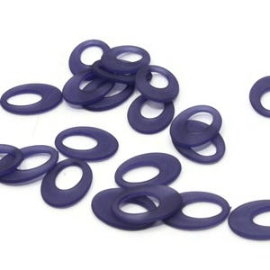 Puede incluir: Un grupo de 15 anillos de plástico ovalados de color morado con un agujero en el centro. Los anillos están dispersos sobre una superficie blanca.