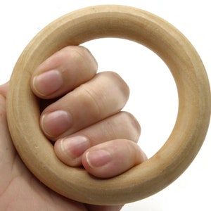 May include: A light-colored wooden ring held in a hand. The ring is smooth and appears to be made of a light-colored wood. The hand is holding the ring, with the fingers curled around it.