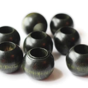 May include: A group of eight black wooden beads with a hole in the centre. The beads have a slightly green tint and a smooth, polished finish.