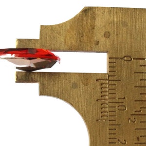 May include: A red glass heart-shaped rhinestone measured with calipers. The calipers show a measurement of 1.2 cm.