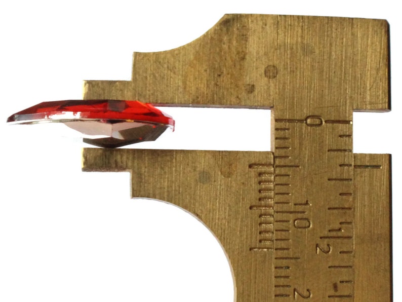 May include: A red glass heart-shaped rhinestone measured with calipers. The calipers show a measurement of 1.2 cm.