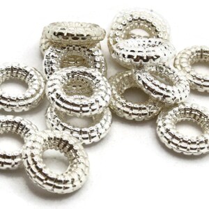 May include: A group of silver-toned metal rings with a textured surface. The rings are all the same size and shape, and they are arranged in a pile.