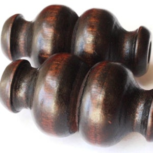 Może przedstawiać: Dwa ciemnobrązowe drewniane koraliki o kształcie bańki. Koraliki mają gładkie, polerowane wykończenie i lekko czerwonawy odcień.