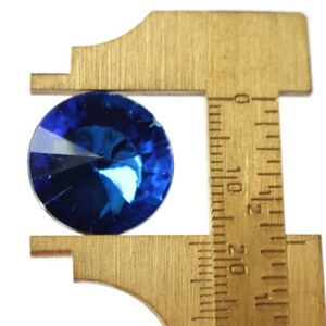 May include: A blue gemstone is being measured with a brass caliper. The caliper has markings in inches.