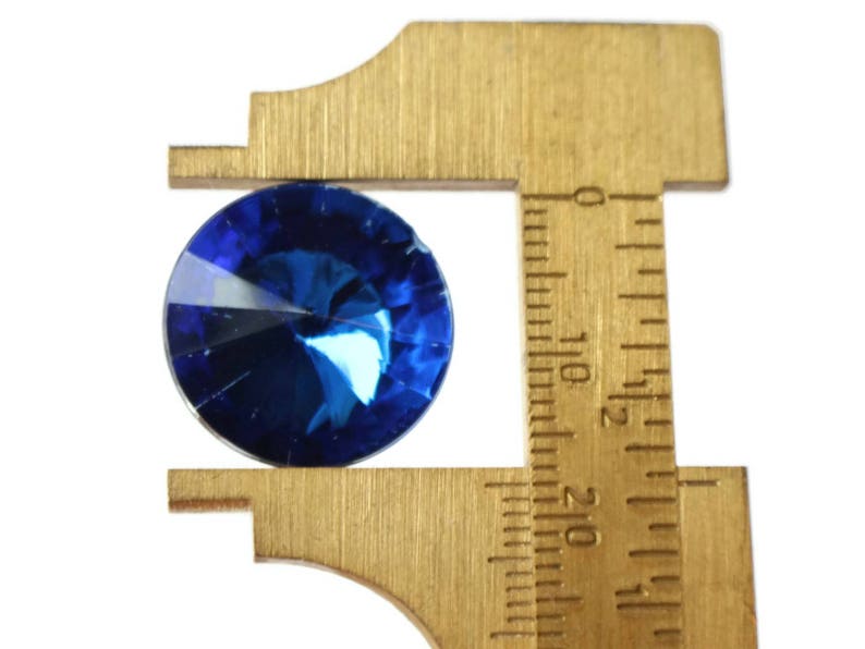 May include: A blue gemstone is being measured with a brass caliper. The caliper has markings in inches.
