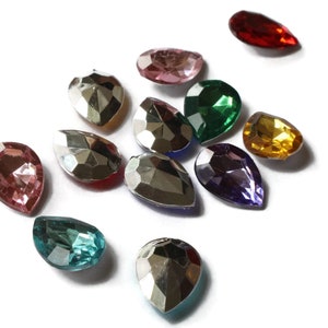 May include: Assortment of teardrop-shaped glass rhinestones in various colors, including red, pink, green, purple, gold, and silver. The rhinestones are faceted and have a shiny finish.