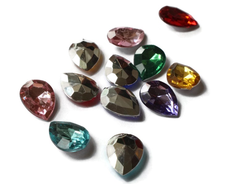 May include: Assortment of teardrop-shaped glass rhinestones in various colors, including red, pink, green, purple, gold, and silver. The rhinestones are faceted and have a shiny finish.