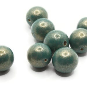 May include: A collection of teal-colored, round beads with a metallic gold speckled finish. Each bead has a small hole for stringing. The beads are scattered on a white surface, ideal for jewelry making or craft projects.