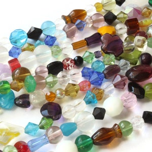 May include: A collection of colorful glass beads in various shapes and sizes, including round, square, and teardrop. The beads are made of clear, opaque, and iridescent glass.