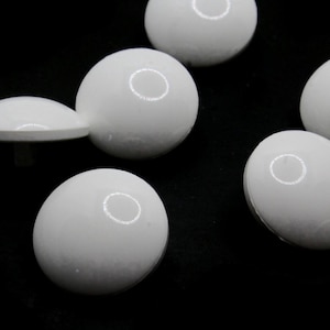 May include: Six white round buttons with a smooth, glossy finish. The buttons are arranged in a semi-circle on a black background.