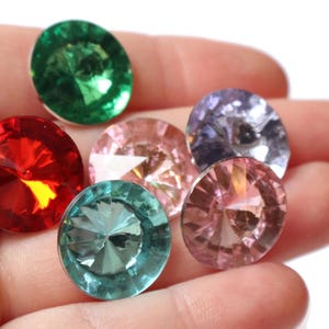 May include: Six round, faceted, glass gems in various colors, including red, green, pink, and purple. The gems are arranged in a semi-circle on a hand.
