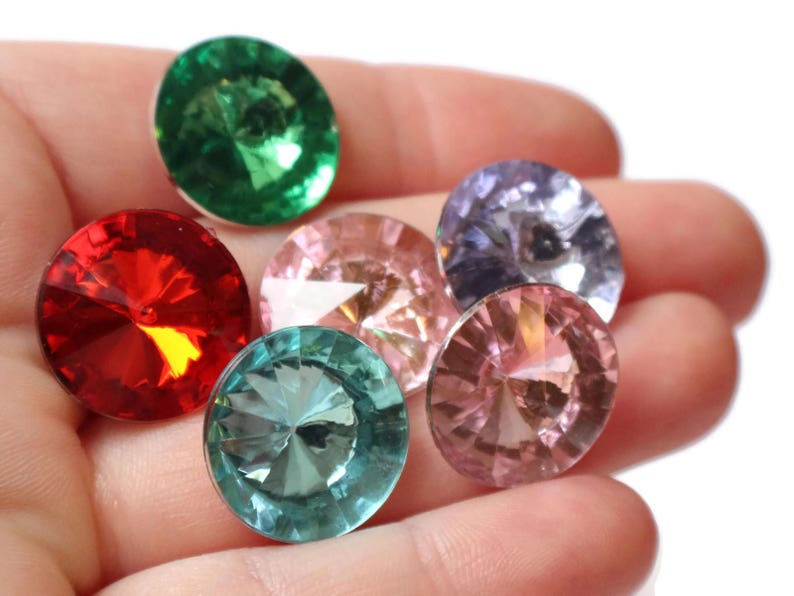 May include: Six round, faceted, glass gems in various colors, including red, green, pink, and purple. The gems are arranged in a semi-circle on a hand.
