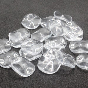 May include: A group of clear plastic buttons, some are oval shaped and some are round. The buttons have a small hole in the centre.