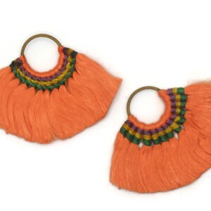 May include: A pair of orange tassel earrings with a woven band of green, purple, and yellow thread. The earrings are made with a brass hoop.