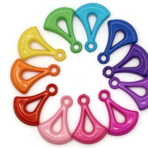Puede incluir: Un conjunto de 12 abalorios de plástico de colores vivos en forma de abanico con un agujero en el centro. Los abalorios están dispuestos en círculo, cada abalorio es de un color diferente del arcoíris.