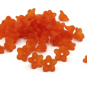 May include: A pile of orange flower-shaped beads. The beads are made of plastic and have a frosted finish.